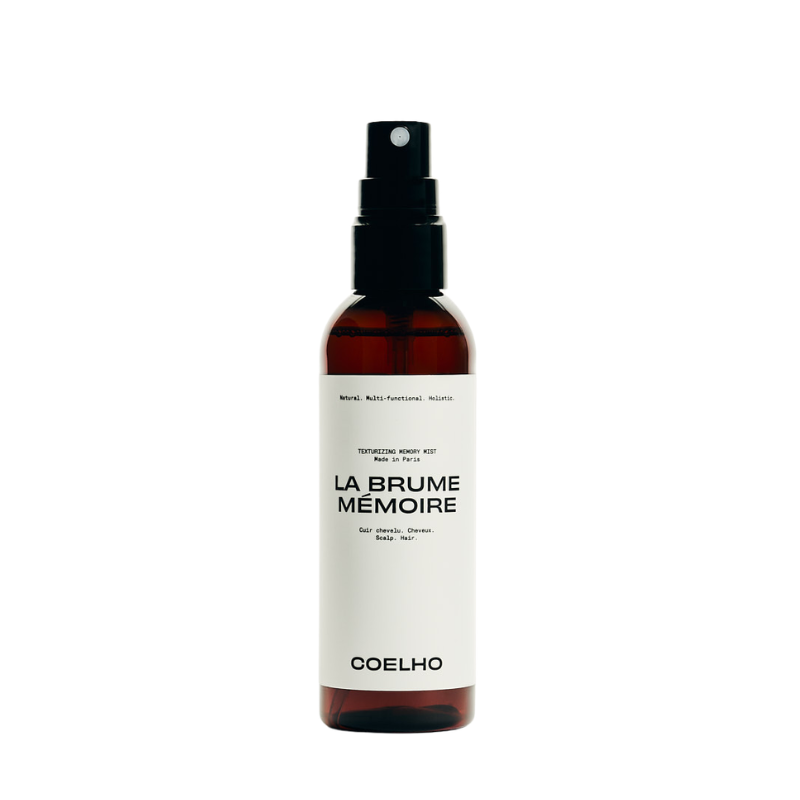 A 100ml amber spray bottle with a black pump dispenser and a white label. The label features the brand name 'COELHO' and the scent name 'LA BRUME MÉMOIRE' in black text.