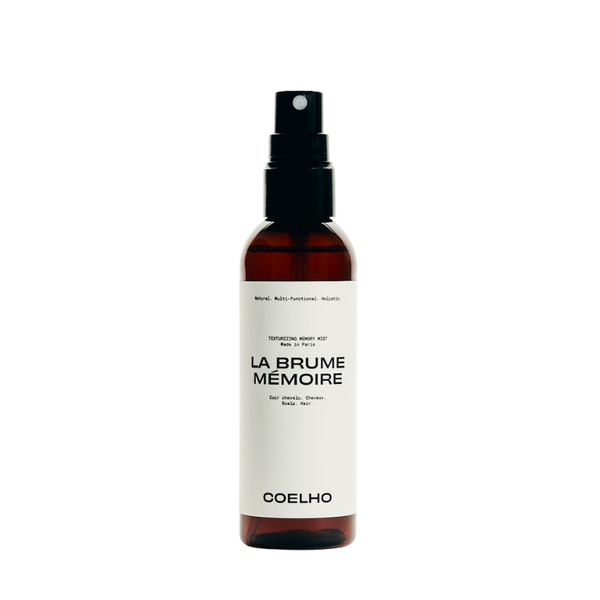 A 100ml amber spray bottle with a black pump dispenser and a white label. The label features the brand name 'COELHO' and the scent name 'LA BRUME MÉMOIRE' in black text.