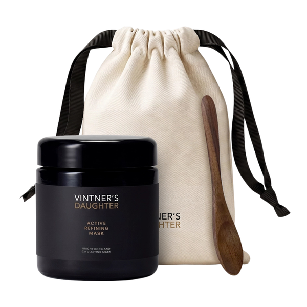 Vintner's Daughter Active Refined Mask set featuring a black jar of the mask, a cream-colored drawstring pouch with black ribbon straps, and a wooden spoon, all on a solid white background.
